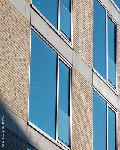 Modern building facade with large windows reflecting clear blue sky during daylight