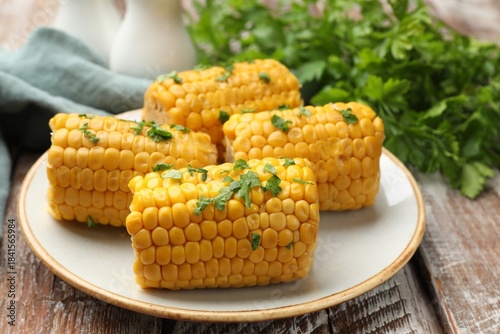 Foto Pieces of boiled corncobs with parsley on wooden table, closeup
