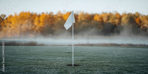 Close-up of a white golf flag on a frosted course with golden autumn trees in the background, seasonal change