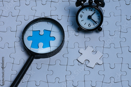 Magnifying glass focusing on puzzle gap with piece beside it and mini alarm clock, symbolizing ready solutions and problem solving before deadline. 