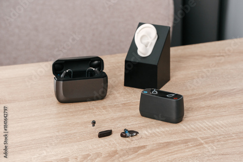 Close-up of modern hearing aids with charging accessories, modern sound and hearing solutions on wooden table in audiology clinic. Ear model for fitting and demonstration.