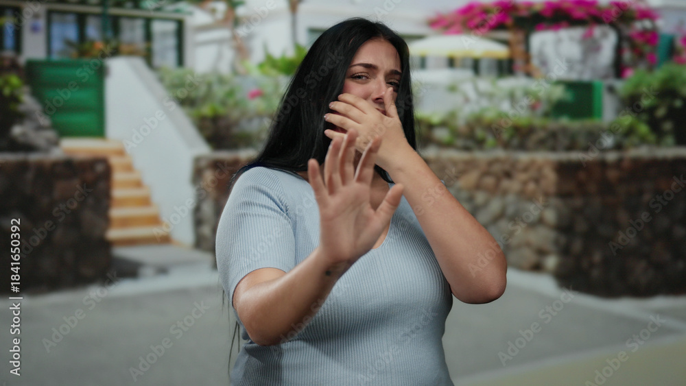 Fototapeta premium Woman covering face with hand outdoors, appearing scared, standing on city street, dressed casually, long hair, with curvy figure, capturing an emotional, urban moment.