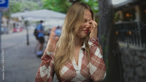 Foto Blonde woman pinches nose with fingers and waves hand for distance on crowded street; disgust aversion avoidance repulsion