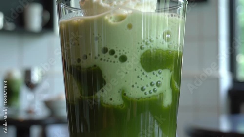 Ultra close-up of iced matcha float with vanilla ice cream melting into vivid green tea. Bubbles cling to glass walls in cool crisp café lighting. Refreshing dessert drink texture details.
