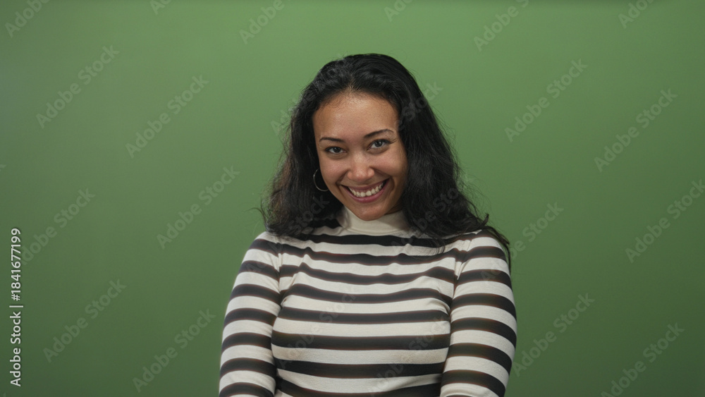 Obraz premium Woman smiling, showing teeth in studio against green wall and striped turtleneck; confidence warmth approachability.