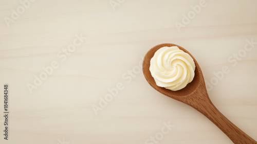 Swirled butter cream sits on wooden spoon against light neutral background