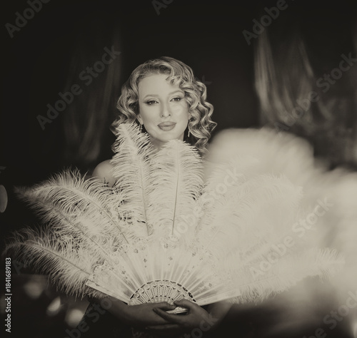 black and white color photo Beauty blonde hair retro lady looking into mirror hand holding fan natural ostrich feathers. sexy woman burlesque show actress. Flapper girl 20s roaring twenties old style