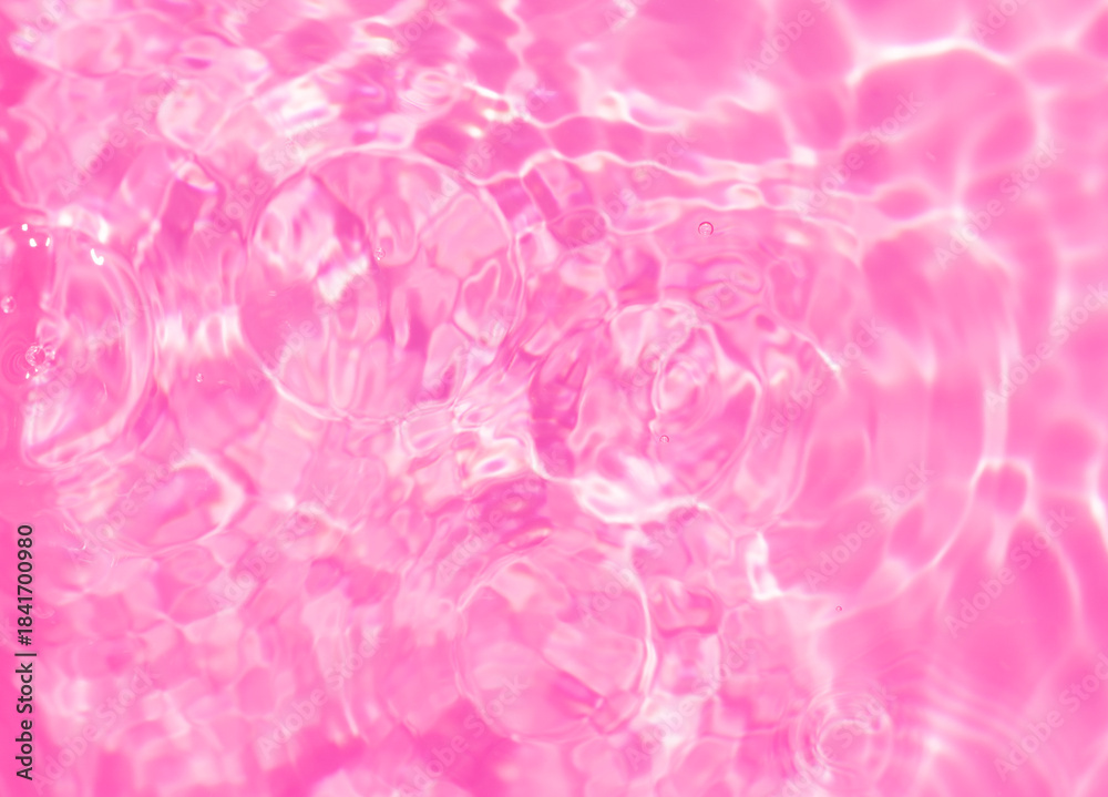 Fototapeta premium Close-up of calm pink clear water surface with water spray and bubbles. Trendy abstract summer nature background. Coral waves in sunlight