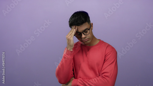 Fotografie Young man in a red sweater with glasses appears worried against a purple background, highlighting his thoughtful and pensive expression