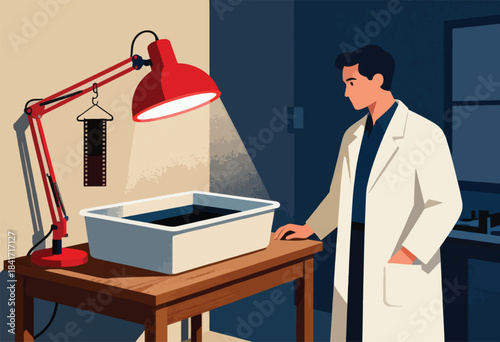 Man in lab coat works with film developing tray under a red lamp
