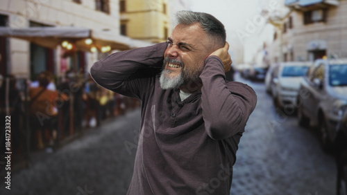 Foto Man covering ears with hands and wincing on a street terrace outside a restaurant; noise discomfort