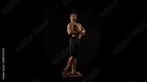 A bodybuilder poses against a black background