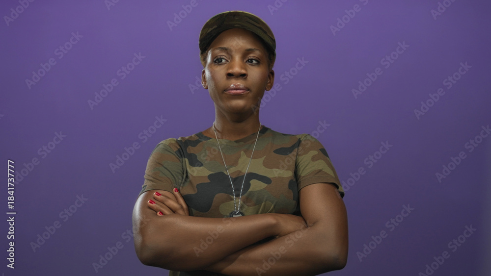 Obraz premium Woman in camouflage uniform crosses arms showing military dog tags in studio and gazes ahead with a stoic expression; pride.