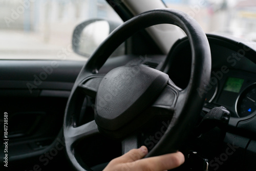 A hand grips the steering wheel of a car on a busy street in the city