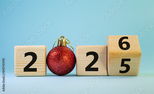 2026 New Year symbol. Businessman turns wooden cube and changes Year 2025 to 2026. Beautiful light blue background with Christmas ball. Copy space. Business and 2026 happy new year concept