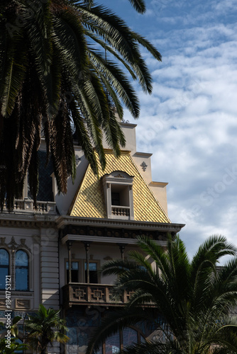 Historic palace-style building with domes and palm trees under cloudy sky