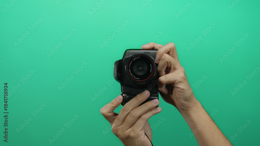 Naklejka premium Man holding camera against green wall background showcases a close-up of hands handling photographic equipment in an isolated studio setting.