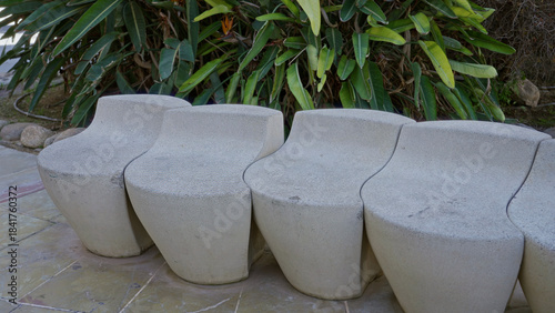 Photography Outdoor scene features modern concrete benches on a sunny day surrounded by lush greenery, providing a peaceful and serene public seating area