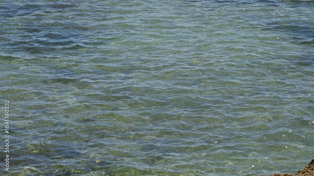 Fototapeta premium Clear turquoise water gently rippling under sunny skies in a tranquil mediterranean sea setting outdoors during a bright day.
