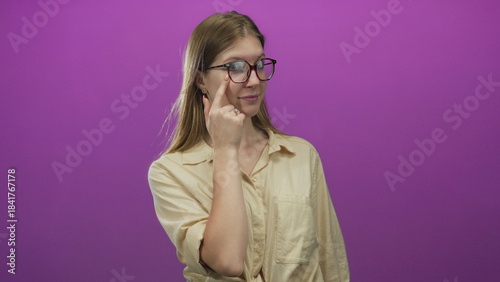 Foto Blonde woman adjusting round glasses with slight smile by pointing finger to lens in purple studio setting; contemplation