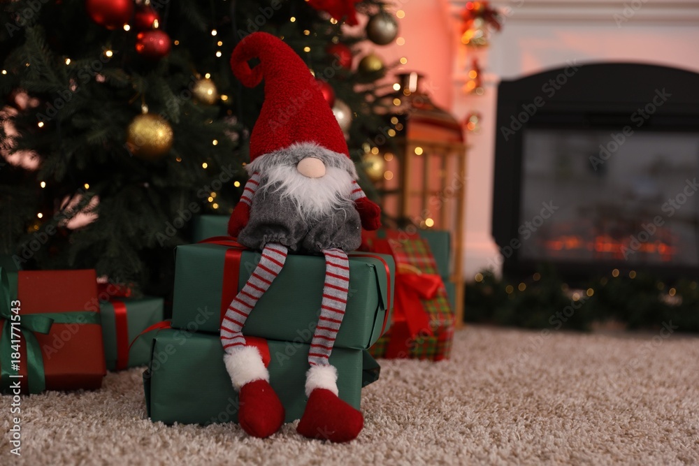 Obraz premium Cute Christmas gnome on gift boxes under fir tree indoors, closeup. Space for text