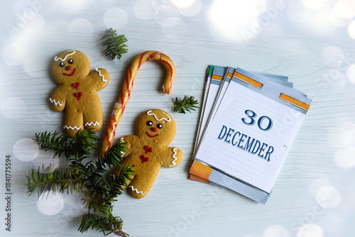 December 30th Calendar: the number 30, the month's name in English, on a flip calendar surrounded by gingerbread cookies, fir branches, and bokeh