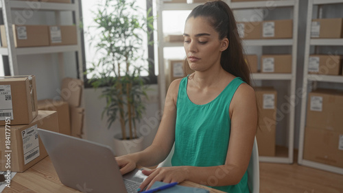 Woman typing on laptop with bare forearm next to stacked boxes in building; entrepreneurial confidence. Free Download Woman typing on laptop with bare forearm next to stacked boxes in building; entrepreneurial confidence. - GFXLoad