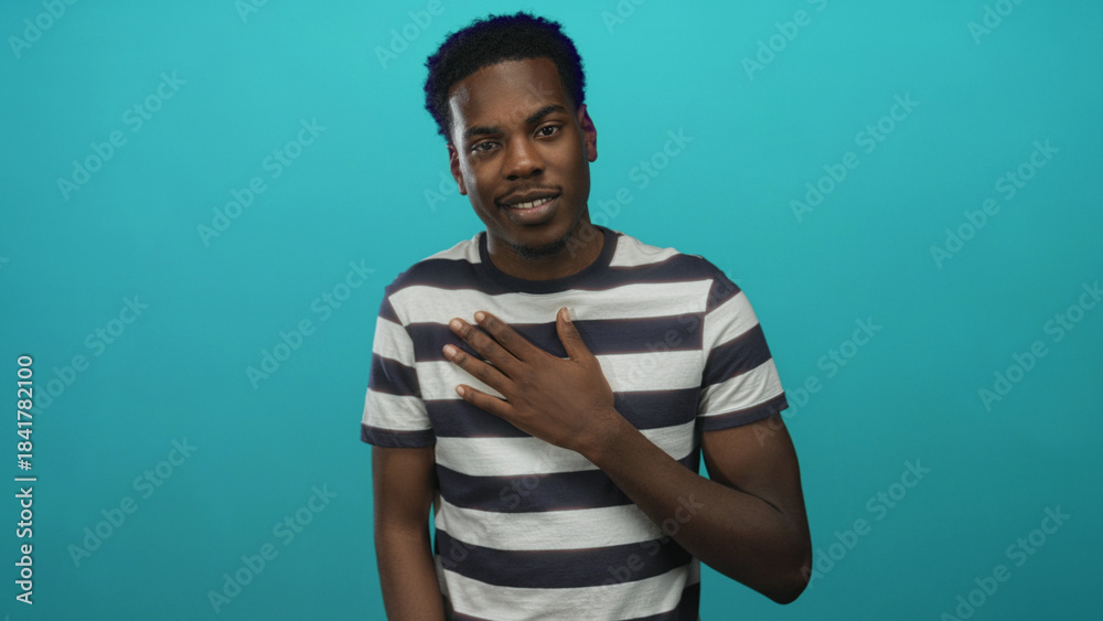Fototapeta premium Young african american man with hand on chest gesture in teal studio; sincerity trust affirmation hope.