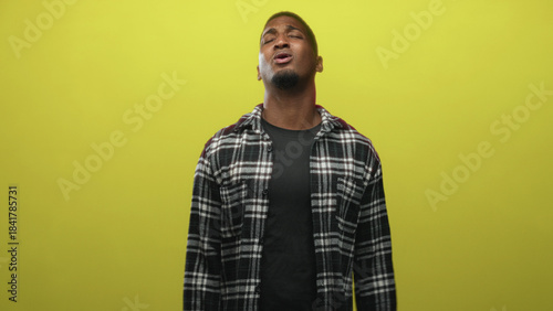 Billede på lærred Young black man holding electric screwdriver with outstretched arms against yellow studio backdrop, eyes closed and expressive; contemplation