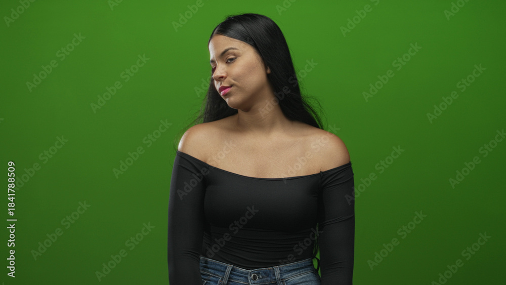 Naklejka premium Woman turning head with bare shoulders in front of green screen in studio under soft lighting; contemplation reflection.