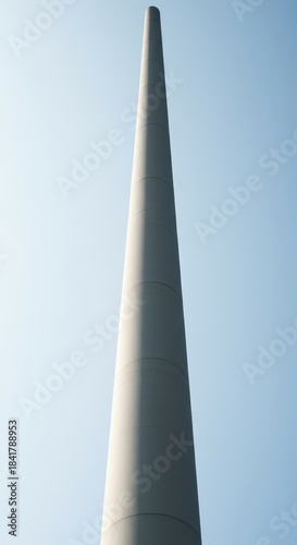 A minimalist view of an extremely narrow, elongated pillar rising vertically against a bright sky, emphasizing its striking thinness and height ,slight ,fragility ,geometry