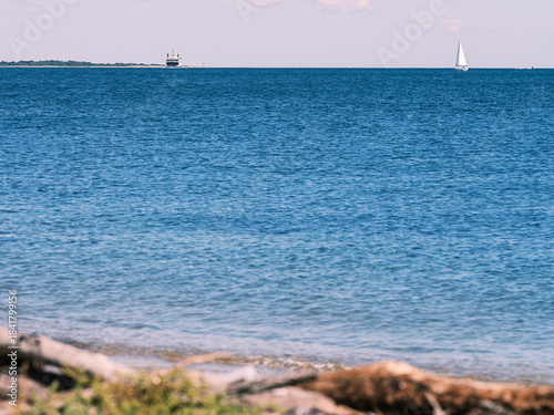 Sailboat on open water with distant ferry on a calm summer day