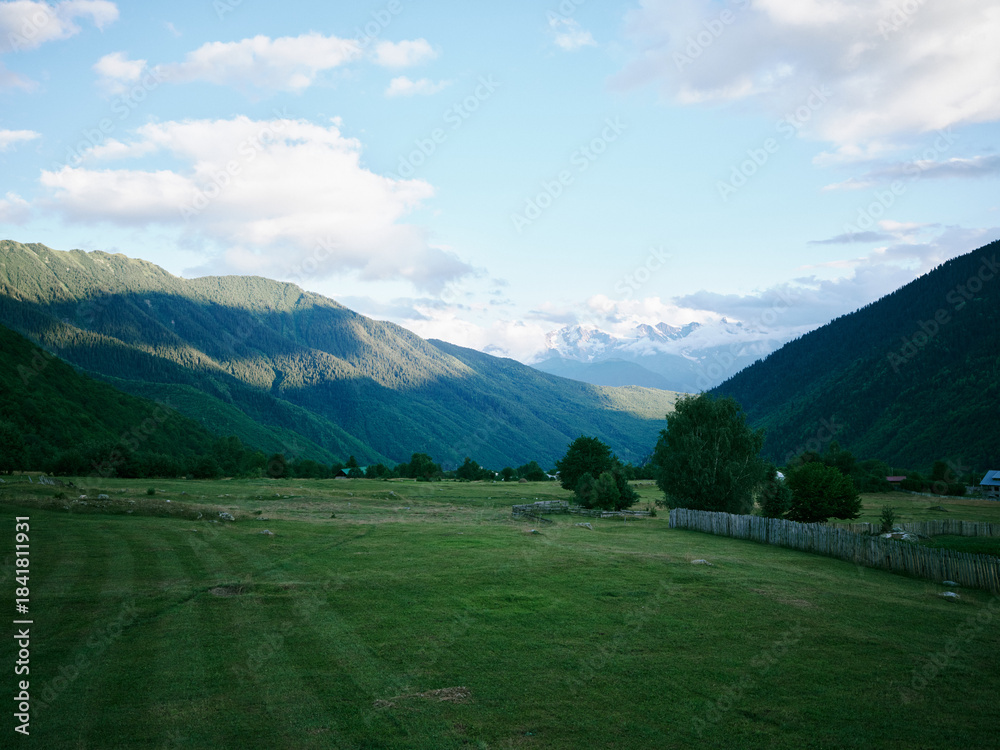 Naklejka premium Landscape valley mountains countryside with expansive fields and greenery under a sky with scattered clouds, creating a tranquil meadow scene in open rural scenery