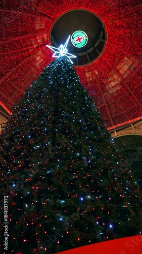Albero di Natale. People take photos near the Lenovo Motorola Christmas tree at the Vittorio Emanuele II luxury shopping mall. festivities. colorful lights. Piazza Duomo. Milan Italy 16.12.2025