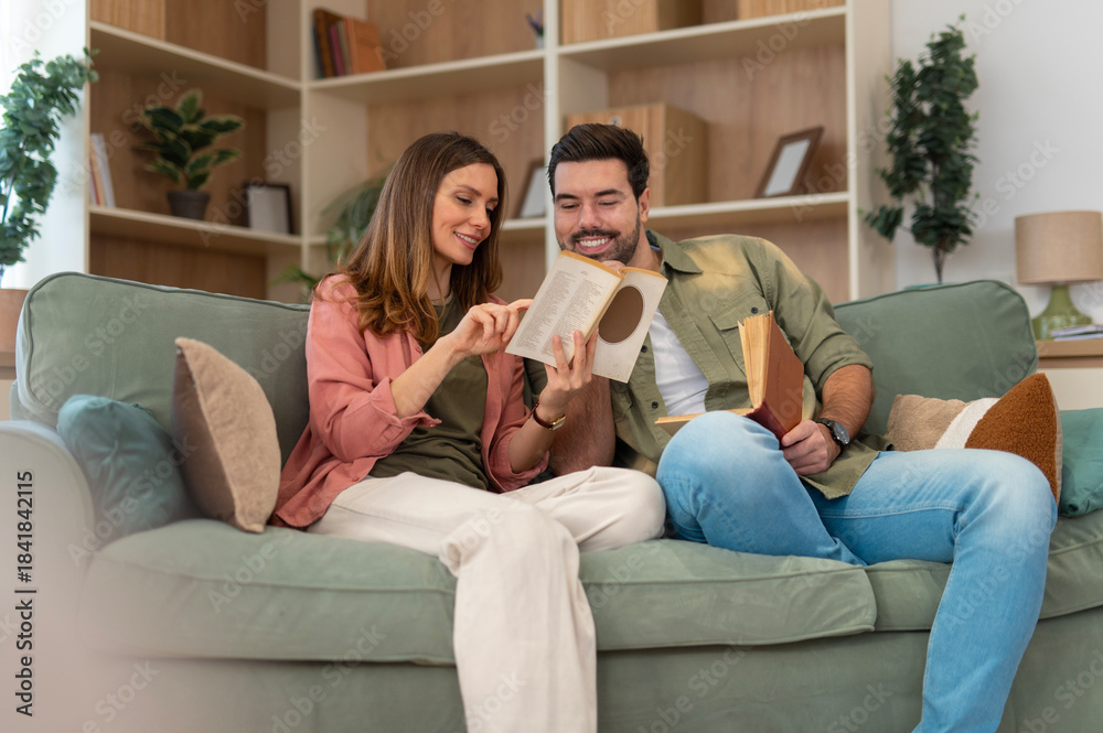 Obraz premium Couple relaxing on sofa reading book together at home