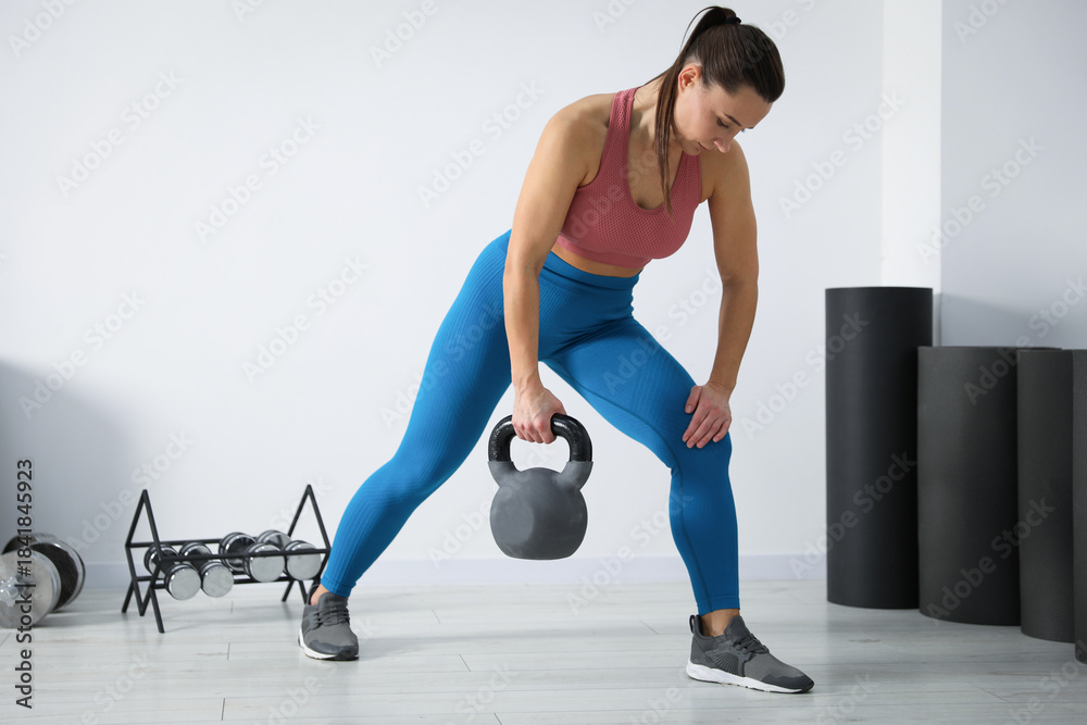 Fototapeta premium Athletic woman exercising with kettlebell near white wall in gym