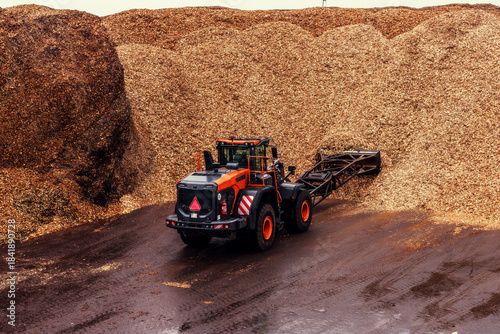 Foto Industrial loader working with large piles of wood chips at a processing facility