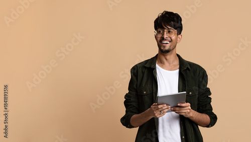 Fotografía A smiling young man stands confidently holding a tablet in his hands, dressed casually