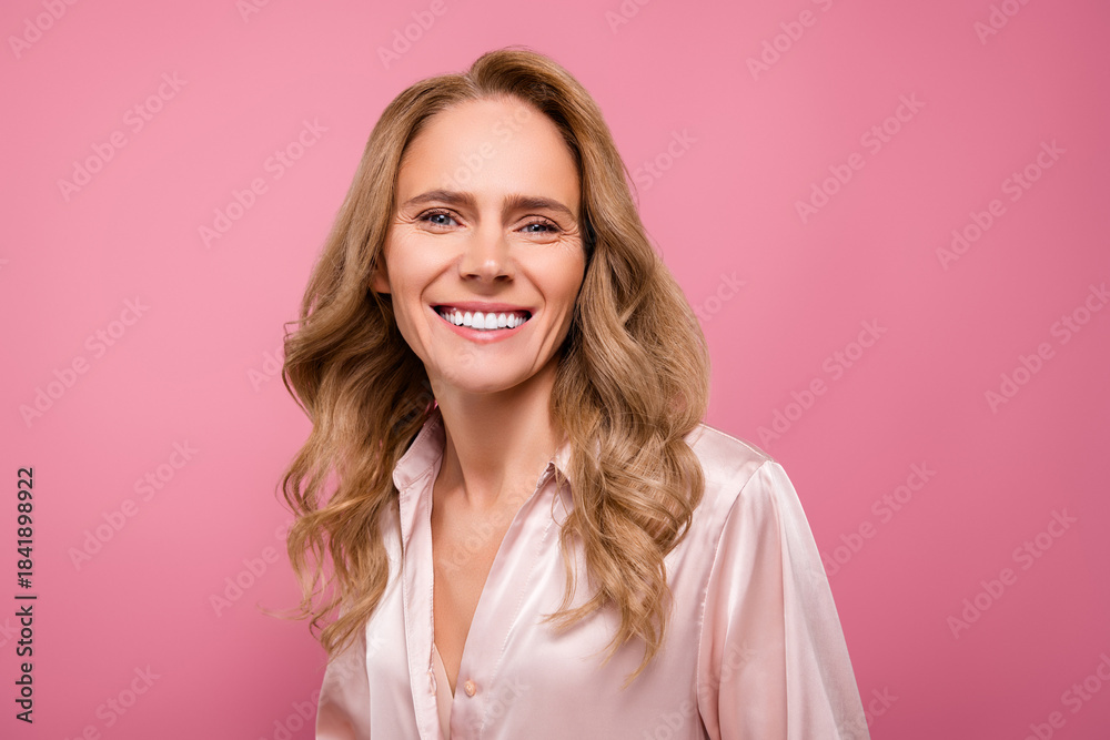 Fototapeta premium Charming mature woman smiling confidently on a pink background, promoting beauty, confidence, and natural skincare