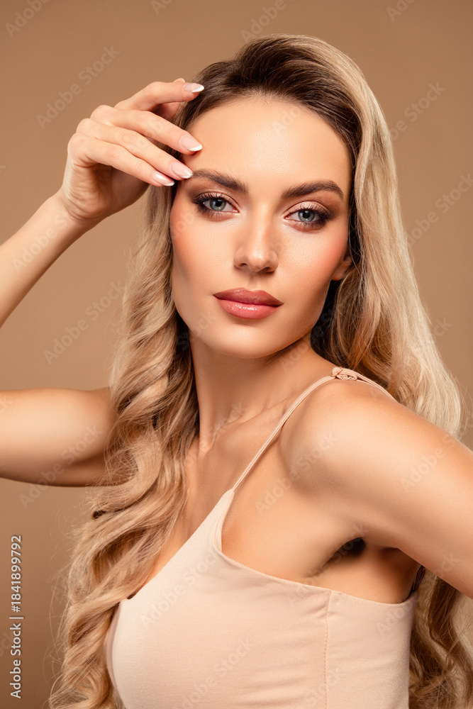 Fototapeta premium Elegant blonde woman with glamorous makeup posing against a beige vertical background showcasing beauty