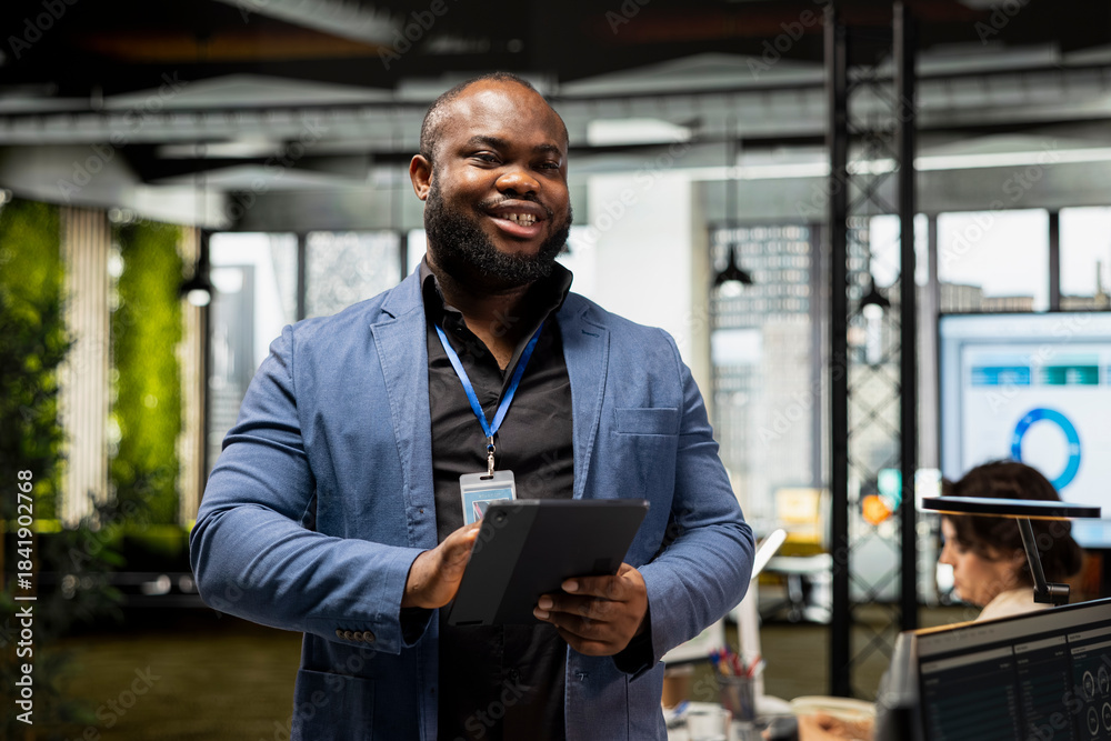 Fototapeta premium Portrait of african american smiling worker does forecasting on his tablet, working in professional corporation office. Using multinational company vision with business solutions for growth.