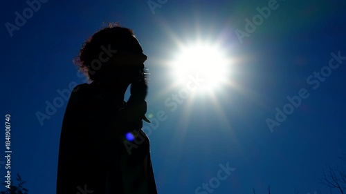 A woman suffers from the heat, waving her hand, making a breeze. Silhouette of a woman against the background of the summer sun