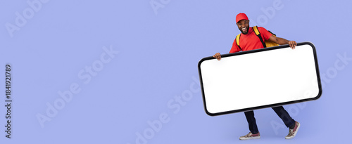 A cheerful young man stands holding a large blank sign, dressed casually in a red shirt and cap. He has a backpack and smiles as he poses for the camera.