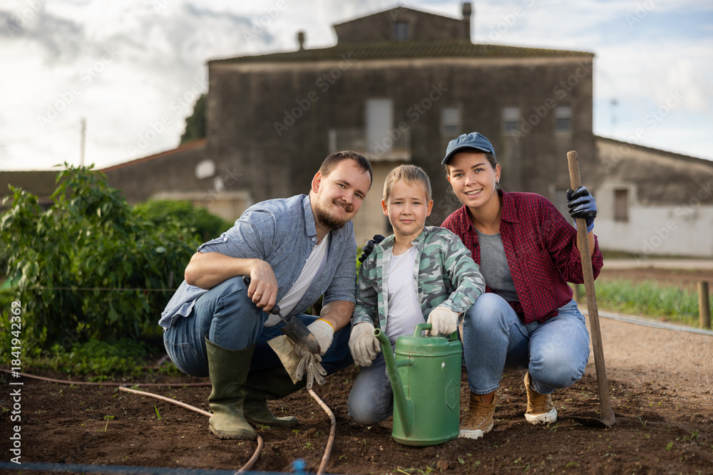 Fototapeta premium Family of farmers with a son in the garden after planting seeds. Generation of farmers grows quality products. Farmers plant seeds in cultivated land