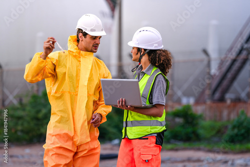 Fotografie Two environmental engineers in PPE gear reviewing field data on a laptop during coastal inspection, focusing on pollution monitoring, water testing, and hazard evaluation