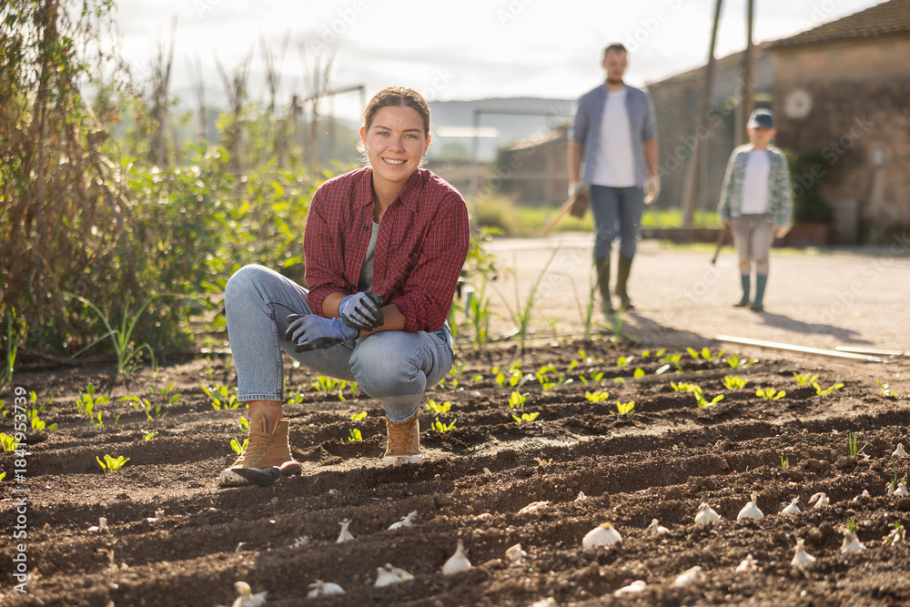 Fototapeta premium Woman farmer planting seeds in the garden on the farm on background of family. Planting seeds and fertilizing the land. Farmer grows organic natural food