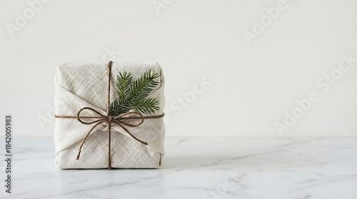 Minimalist gift wrapped in fabric with pine branch on marble surface