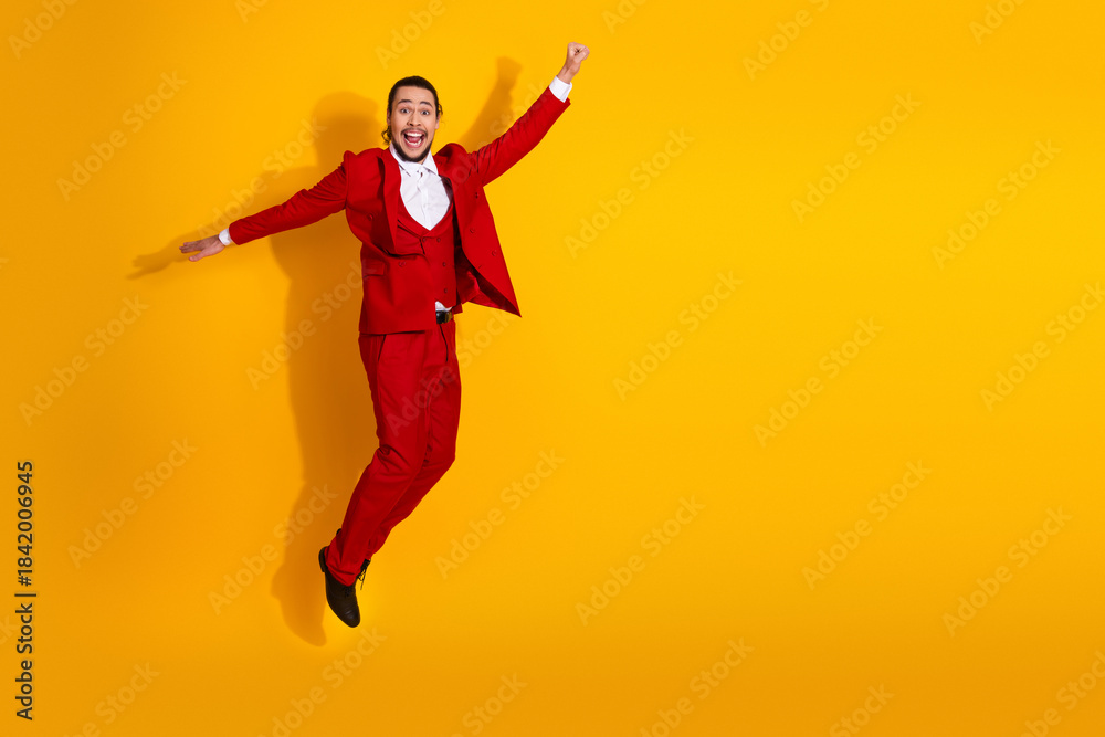 Fototapeta premium Energetic man in red suit leaps against bright yellow background creating a playful dynamic fashion moment perfect for celebration imagery
