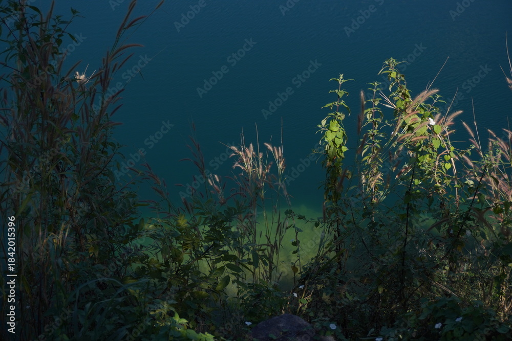 Fototapeta premium Blue Lagoon Phuman Khon Kaen: Majestic gray limestone cliff beside a clear turquoise water pond, with perfect reflection under the summer sky