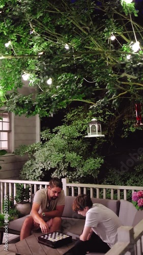 Cozy Summer Night on the Porch – Father and Son Playing Checkers Beneath Glowing String Lights on Cozy Terrace